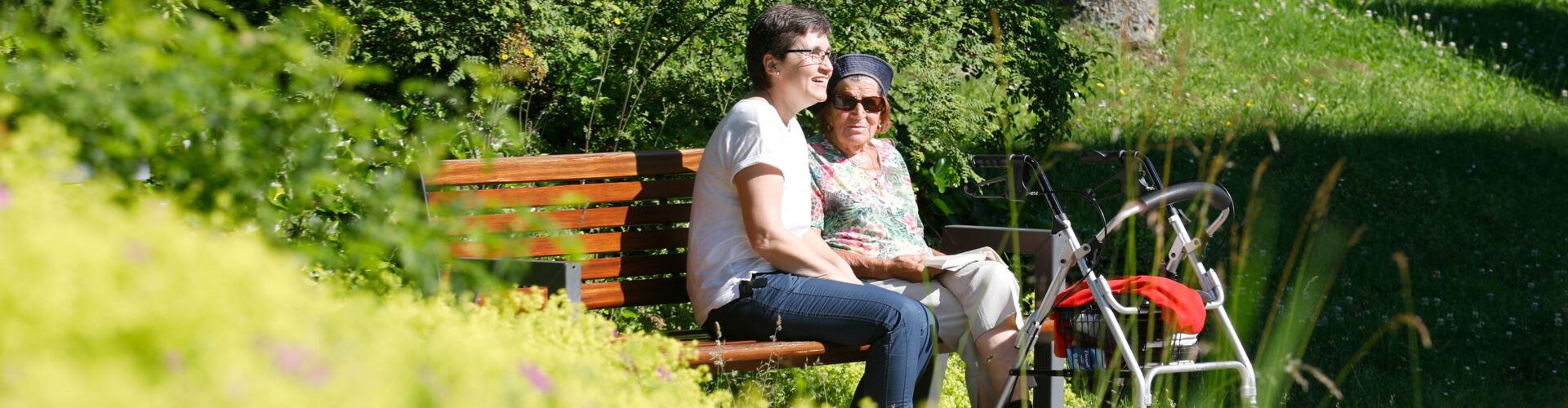 Betreuerin und Seniorin auf einer Bank im Grünen