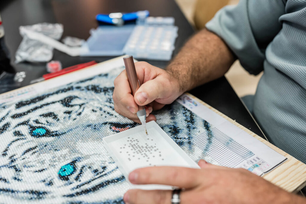 Detailaufnahme des Gemäldes. Es zeigt einen weissen Tiger, der mit Glitzersteinen verziert wird.