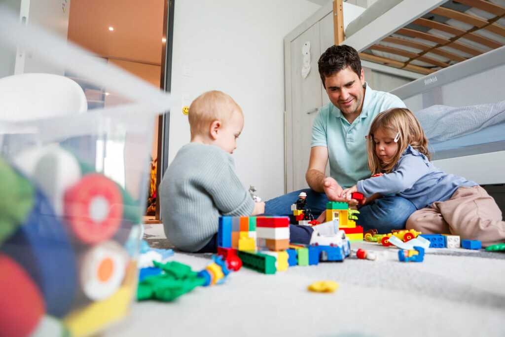 Ein blinder Mann spielt mit seinen zwei kleinen Kindern am Boden im Kinderzimmer.